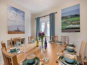 A dining room with a wooden table set for six, featuring teal and white dinnerware, wine glasses, and a bottle of wine.