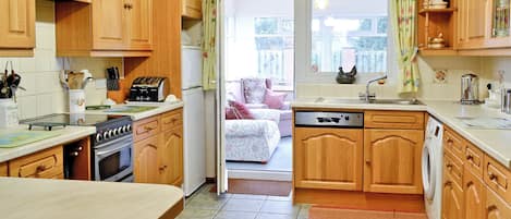 Una cocina con armarios de madera, lavavajillas, estufa y comedor con mesa.