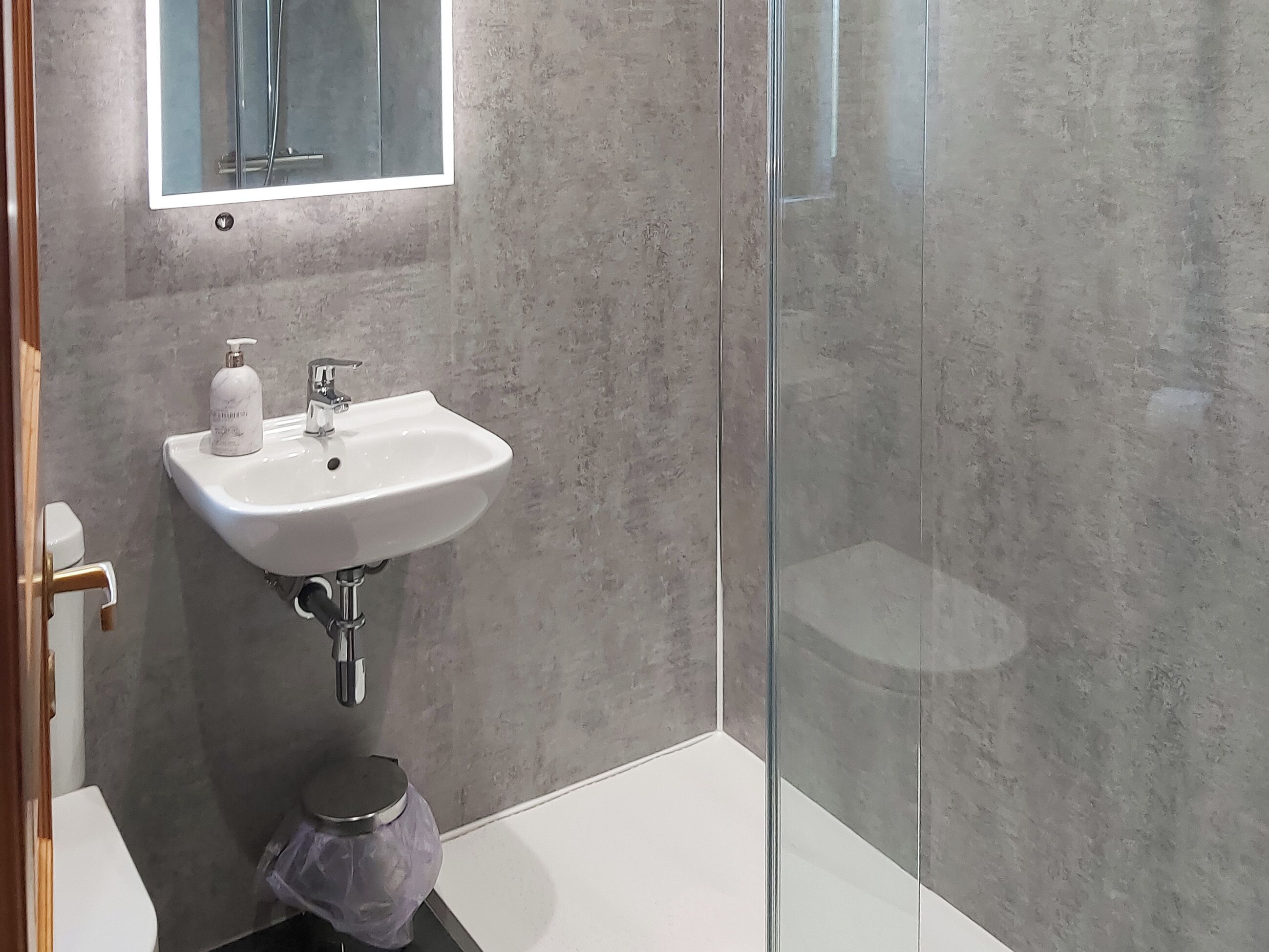 Un baño con lavamanos blanco, un espejo y zona de ducha.