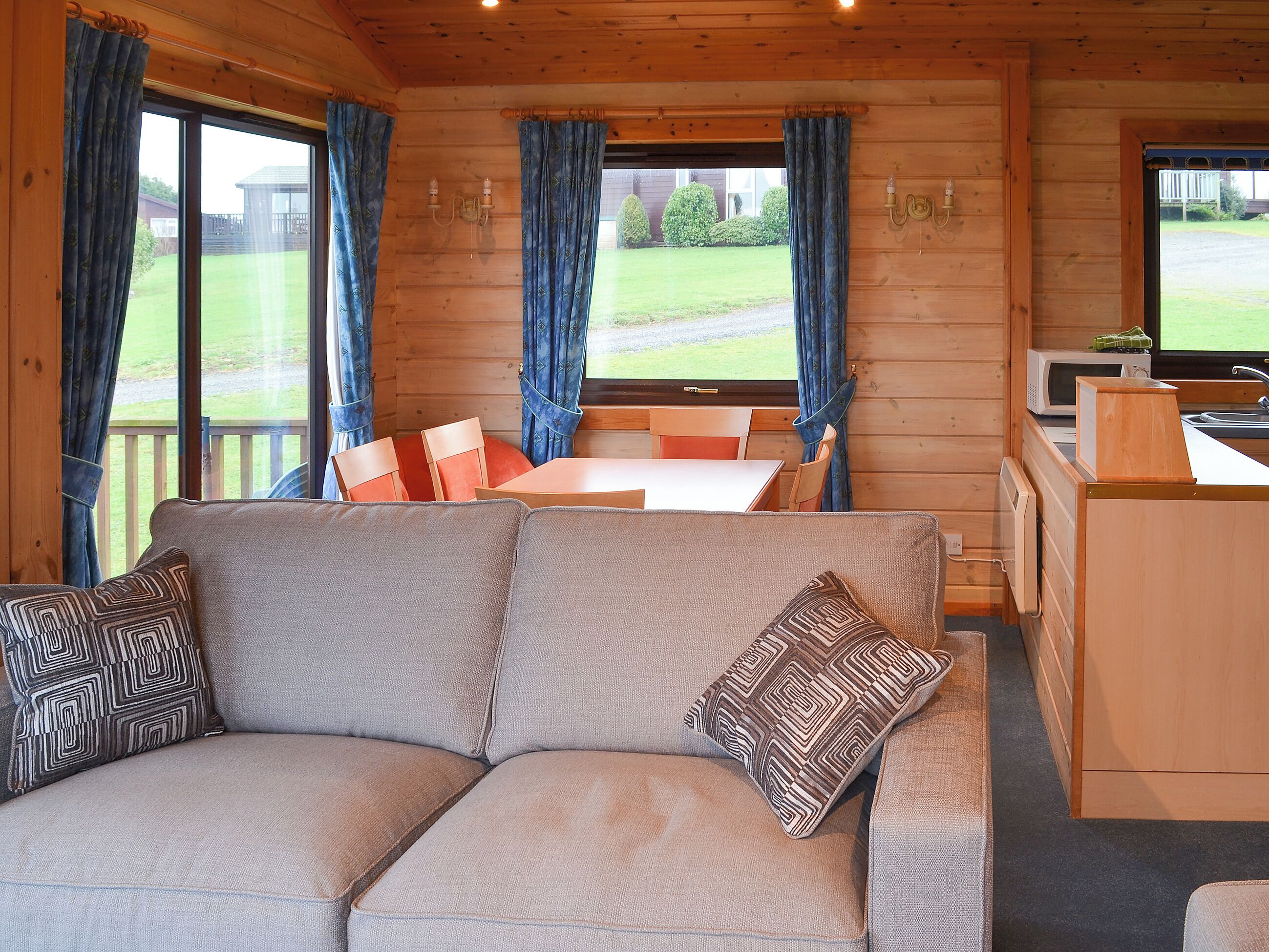 A cozy cabin interior with a sofa, dining table, chairs, and a kitchen area.