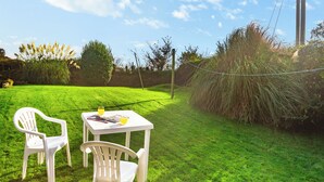 A grassy outdoor area with two white plastic chairs and a small table with a magazine and a glass of juice.