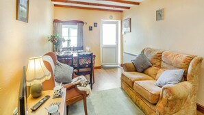 A cozy living room with a wooden ceiling, a dining table set with chairs, a sofa with cushions, and a television.