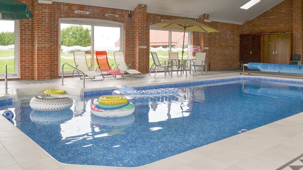 An indoor swimming pool with clear water, lounge chairs, and a brick wall. - Carp Cottage - UKC1907 (Doddington, near Lincoln)