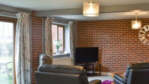 A living room with a brick wall, leather sofas, a TV, and a dining table. - Carp Cottage - UKC1907 (Doddington, near Lincoln)