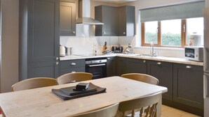 A modern kitchen with dark cabinets, a marble countertop, and a dining table with chairs. - Carp Cottage - UKC1907 (Doddington, near Lincoln)