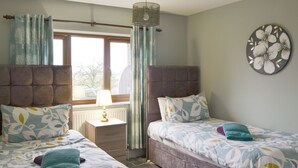 A bedroom with two beds, a nightstand, a lamp, and a window with curtains. - Carp Cottage - UKC1907 (Doddington, near Lincoln)