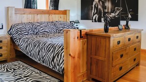 Une chambre à coucher avec un lit en bois, une table de chevet, une commode à tiroirs et un tapis à motifs zébrés.