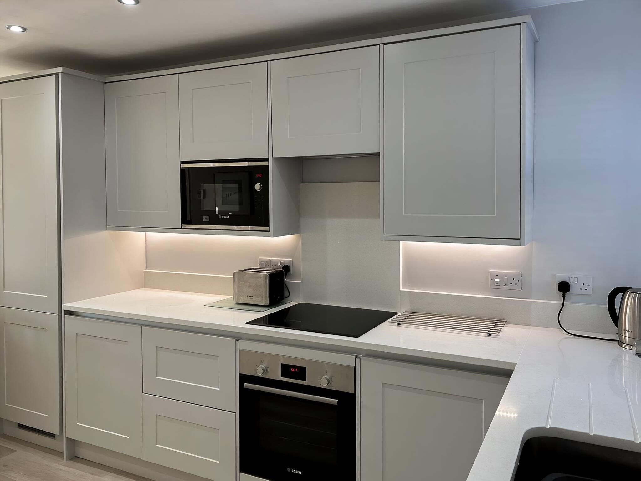 A modern kitchen with grey cabinets, a Bosch microwave, a toaster, and a dishwasher.