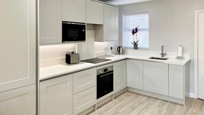 Une cuisine moderne avec des meubles blancs, un four à micro-ondes encastré, un grille-pain, une bouilloire et un évier.
