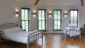 Un dormitorio con dos camas de estructura metálica, suelo de madera y ventanas amplias con persianas.