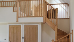 Una habitación amplia con techo alto, una escalera de madera y dos puertas de madera.