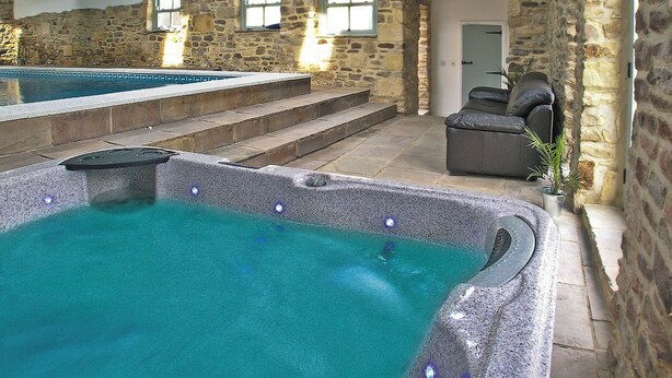 Un área de spa con un jacuzzi y una piscina, paredes de piedra y techo de madera.
