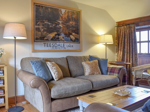 A living room with a sofa, two floor lamps, a framed picture, a wooden coffee table, and a wicker chair.