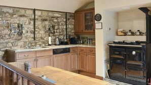 A kitchen with stone walls, wooden cabinets, a wooden countertop, a dishwasher, a stove, and a clock. - The Cottage at Wilson House (Barningham, near Richmond)