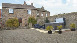 A stone building with a gravel courtyard, outdoor seating, and a large screen. - The Cottage at Wilson House (Barningham, near Richmond)
