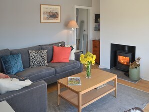 Una sala de estar con sofá, una mesa de centro con una revista, un jarrón con flores, chimenea y un cuadro en la pared.