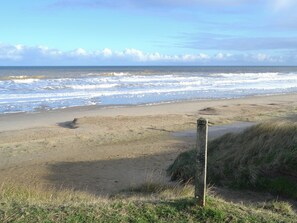 A beach with waves, a sandy shore, and a grassy area with a wooden post.