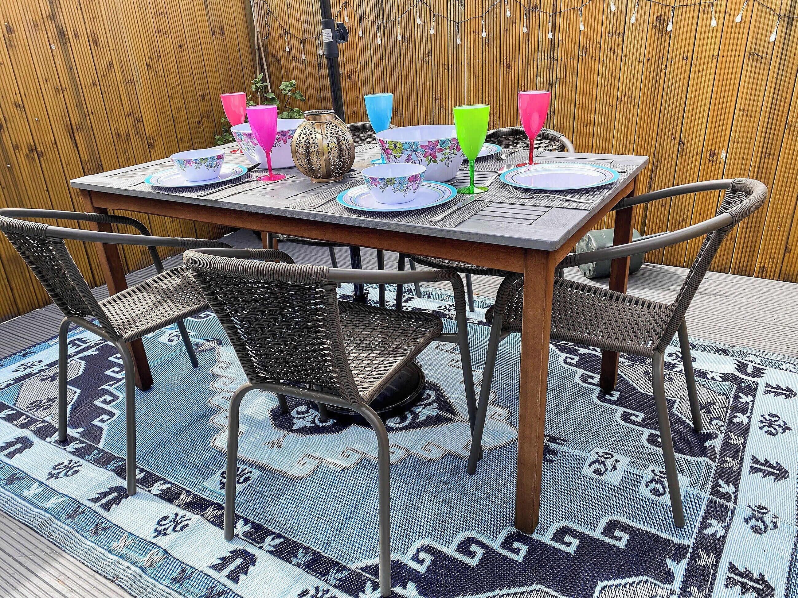 Een eettafel met kleurrijk servies en glazen, omringd door rieten stoelen op een gekleurd vloerkleed.