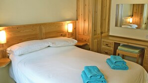 A neatly made bed with white linens, a wooden headboard, and two rolled towels on the bed. - 1 bedroom accommodation in Mevagissey, near St Austell (Mevagissey, near St Austell)
