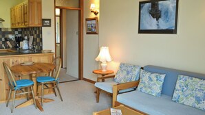 A cozy living area with a sofa, chairs, a coffee table, and a kitchen area with wooden cabinets and a tiled backsplash. - 1 bedroom accommodation in Mevagissey, near St Austell (Mevagissey, near St Austell)