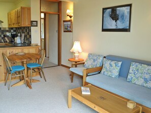A cozy living area with a sofa, chairs, a coffee table, and a kitchen area with wooden cabinets and a tiled backsplash.
