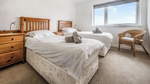 Un dormitorio con dos camas, un aparador de madera, una silla y un ventanal grande.