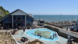 Edifici costaner amb zona de piscina, un cafè i vistes al mar.