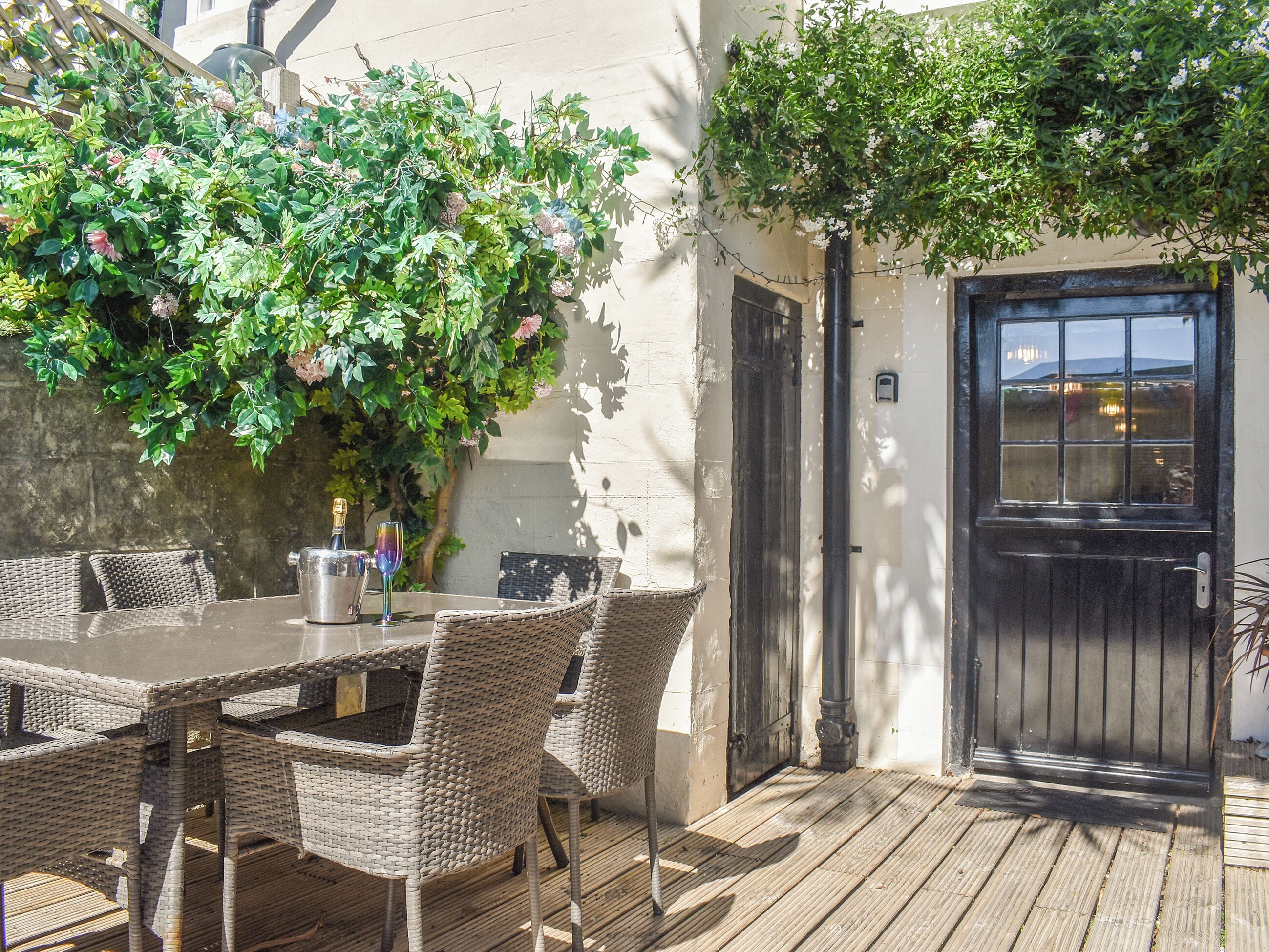 An outdoor patio with wicker furniture, a table with a bottle and glass, and a door with a window.