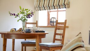 A wooden dining table with chairs, a vase with flowers, a teapot, cups, and a plate with food. - 1 bedroom accommodation in Bleatarn, near Kirkby Stephen (Bleatarn, near Kirkby Stephen)