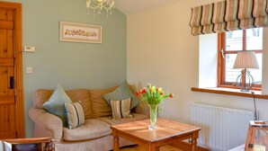 A cozy living room with a beige sofa, a wooden coffee table, a chandelier, a window with curtains, and a framed picture on the wall. - 1 bedroom accommodation in Bleatarn, near Kirkby Stephen (Bleatarn, near Kirkby Stephen)