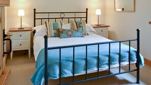 A neatly made bed with a blue blanket, two bedside tables with lamps, a wall-mounted mirror, and a painting above the bed. - 1 bedroom accommodation in Bleatarn, near Kirkby Stephen (Bleatarn, near Kirkby Stephen)