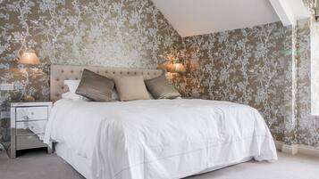 Una camera da letto con testiera trapuntata, un letto con biancheria bianca, due abat-jour e carta da parati con motivi floreali.