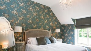 Een slaapkamer met een hemelbed, twee bedlampen, een kroonluchter en een raam met uitzicht op groen.