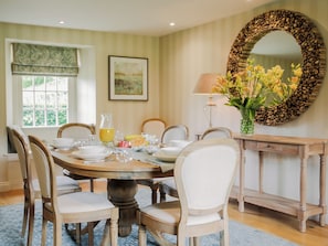 A dining room with a round table, chairs, a vase with flowers, a lamp, and a decorative mirror. - 4 bedroom accommodation in Settrington, near Malton (Settrington, near Malton)