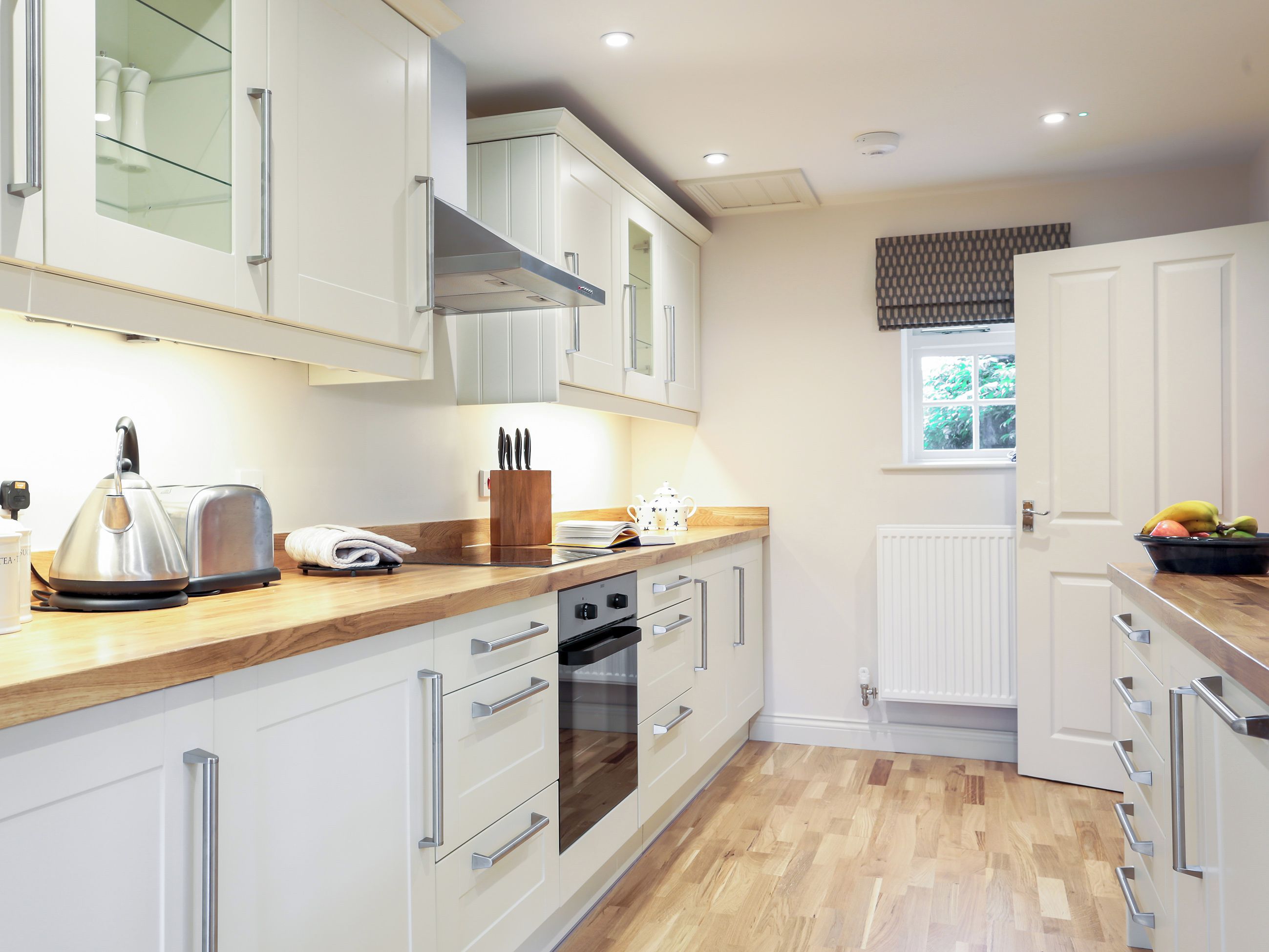 A modern kitchen with white cabinetry, a wooden countertop, a kettle, a toaster, and a fruit bowl.