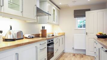 A modern kitchen with white cabinetry, a wooden countertop, a kettle, a toaster, and a fruit bowl.