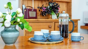 A wooden table with a coffee maker, cups, saucers, and a vase with flowers. - 4 bedroom accommodation in South Tehidy, near Portreath (South Tehidy, near Portreath)