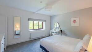 A bedroom with a bed, a bedside table with a lamp, a dresser, a window, a radiator, a mirror, and a framed picture on the wall. - 4 bedroom accommodation in Hawes (Hawes)