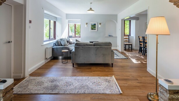 A spacious living area with a grey sofa, a coffee table, and a lamp. There are wooden floors, a rug, and a stone archway. - 4 bedroom accommodation in Hawes (Hawes)