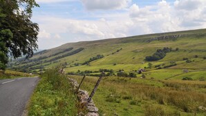 A rural road curving through a hilly landscape with stone walls and sparse vegetation. - 4 bedroom accommodation in Hawes (Hawes)