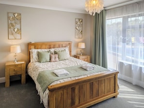 A wooden bed with a green throw, two bedside tables with lamps, and a large window with sheer curtains.