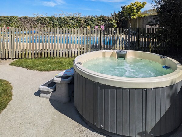 A hot tub with a wooden fence and a pool in the background.