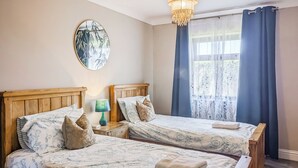 A room with two wooden beds, a round mirror, a nightstand with a lamp, and a window with curtains.