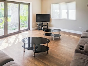 A living room with a TV, two glass tables, a sofa, and a sliding glass door to a garden.