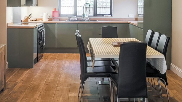 A modern kitchen with a dining area, wooden flooring, and a view of the outdoors.