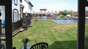 Un patio con una mesa y sillas, un jarrón de flores, césped, un muelle para barcos y un edificio con un letrero al fondo.