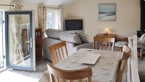 A living room with a sofa, a television, a table with chairs, and a glass door with curtains. - 2 bedroom accommodation in Port Isaac (Port Isaac)