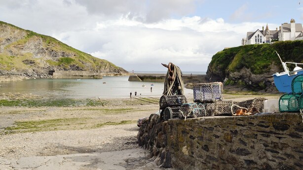 A coastal scene with a rocky shore, a fishing boat, and a building on a cliff. - 2 bedroom accommodation in Port Isaac (Port Isaac)