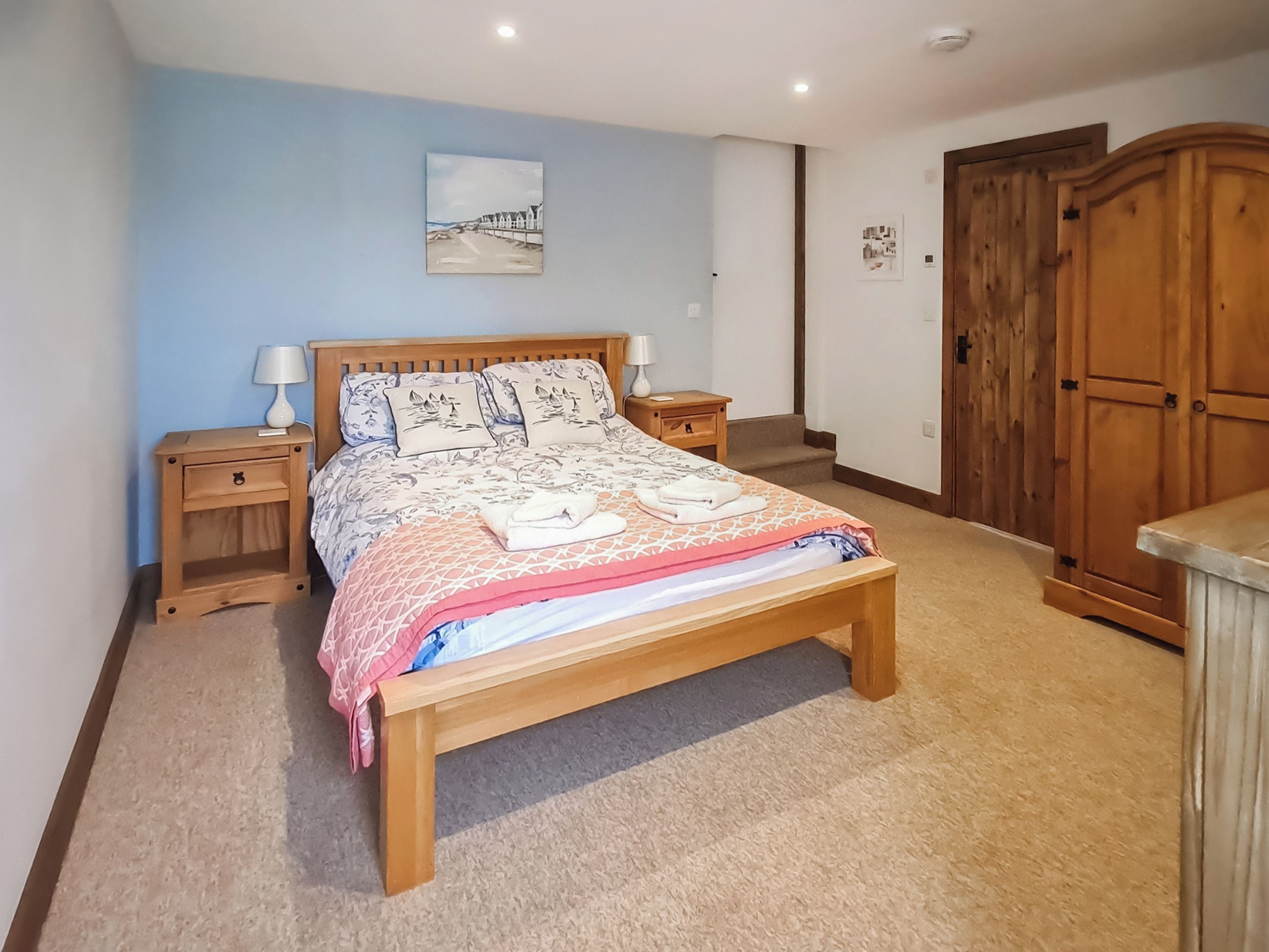 Een slaapkamer met een houten bed, nachtkastjes, een hoofdeinde met een schilderij, een kledingkast en een vloerbedekking.