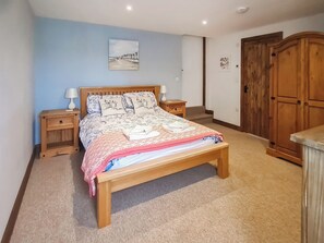 A bedroom with a wooden bed, nightstands, a headboard with a painting, a wardrobe, and a carpeted floor.